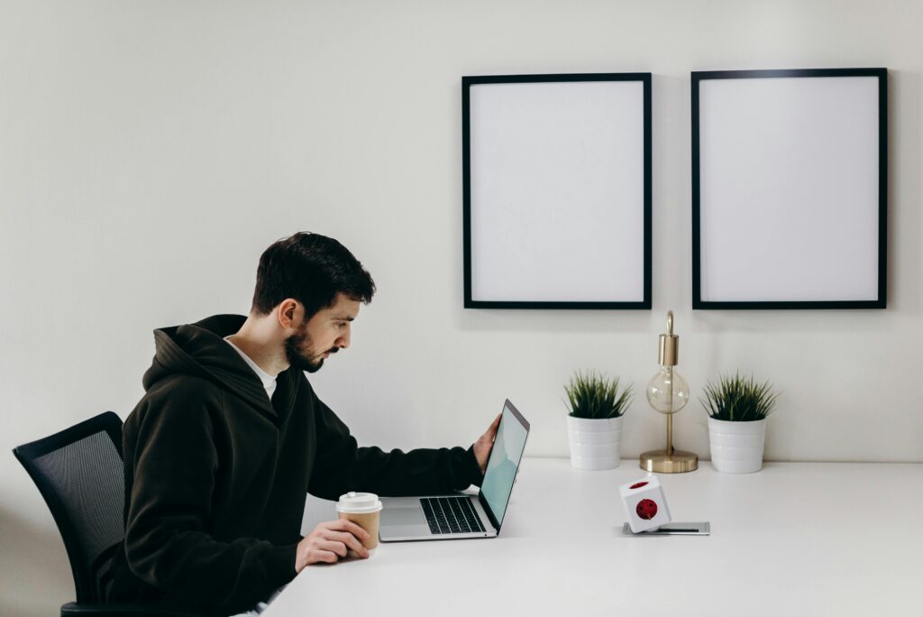 Man working remotely on a laptop at a minimalist desk with coffee cup and plants in a modern home office.