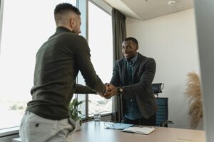 Two businessmen shaking hands across a desk in a modern office, symbolizing partnership and professional agreement.